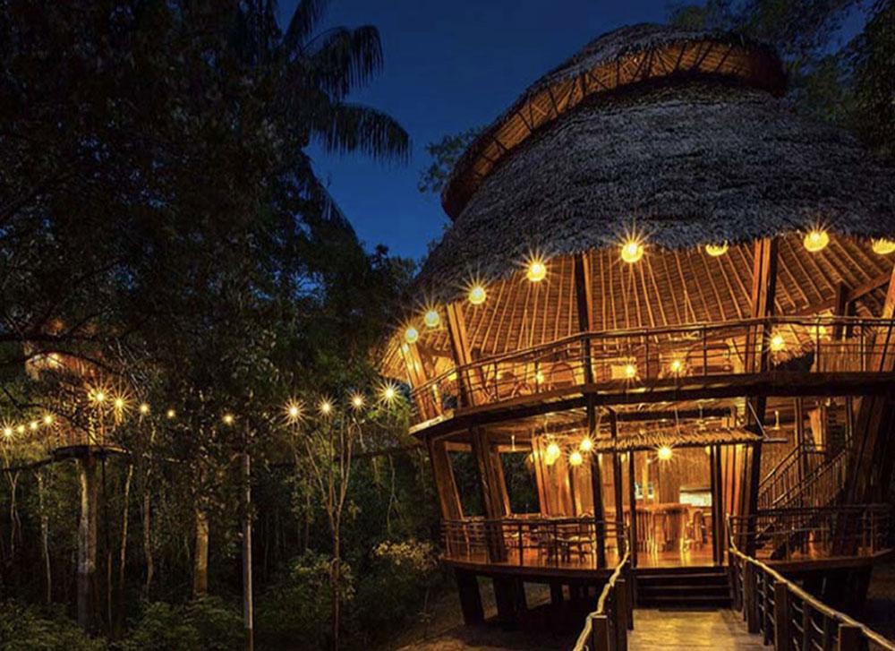 An Amazon Jungle lodge that is being pictured in the evening as the sky is dark. The jungle lodge is built to be mostly outdoors